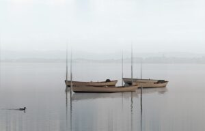Trois petits bateaux de pêche amarrés dans un lac brumeux par temps calme, avec des montagnes floues en arrière-plan